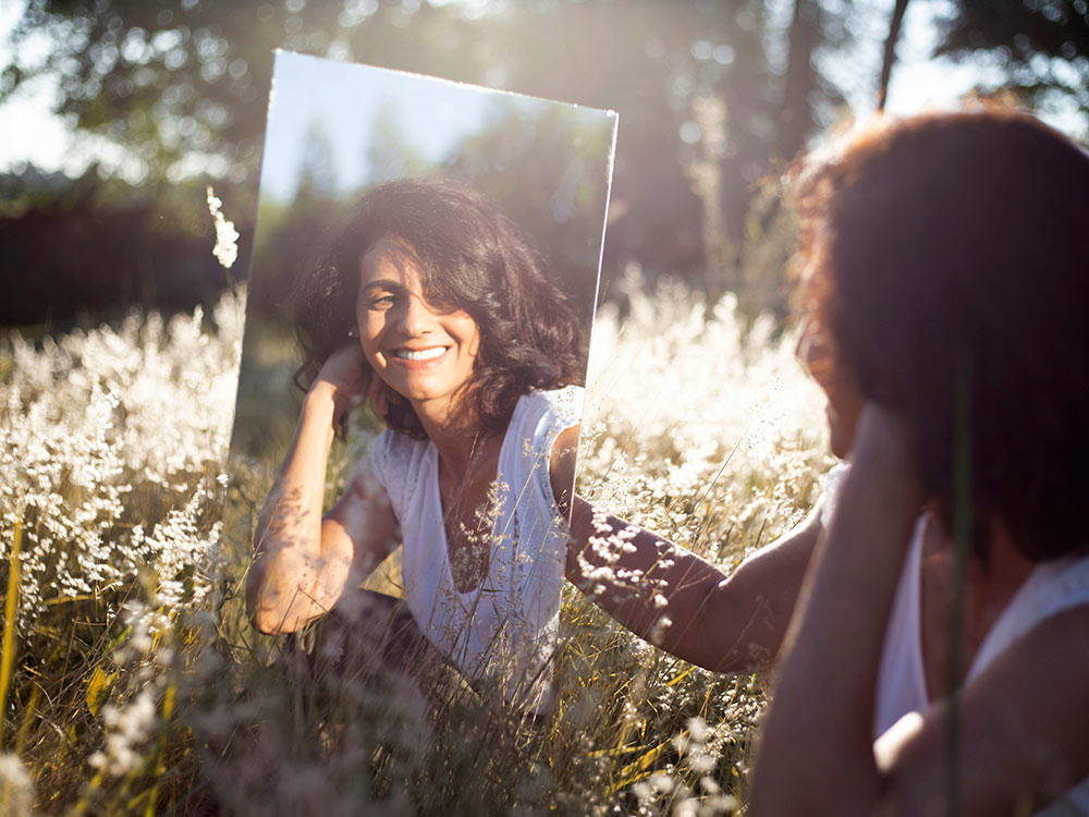 A woman gazes confidently at her reflection in a mirror, embodying self-assurance and empowerment